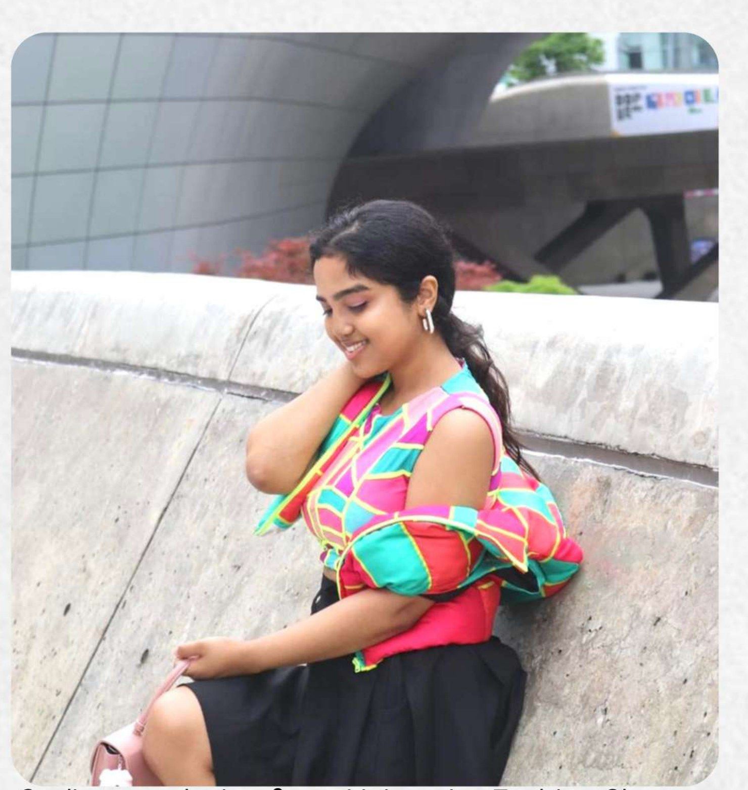 Etosha Paul seated on a concrete ledge outside Dongdaemun Design Plaza, wearing her own patchwork top